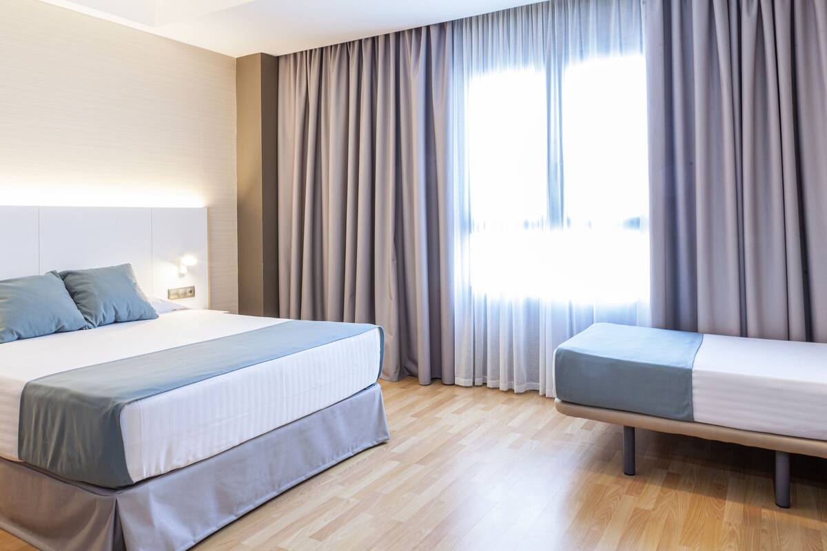 Une chambre d’hôtel avec un grand lit, un lit plus petit et une fenêtre avec des rideaux.