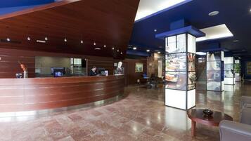 A modern hotel lobby with a curved reception desk, seating area, and a glass display case.