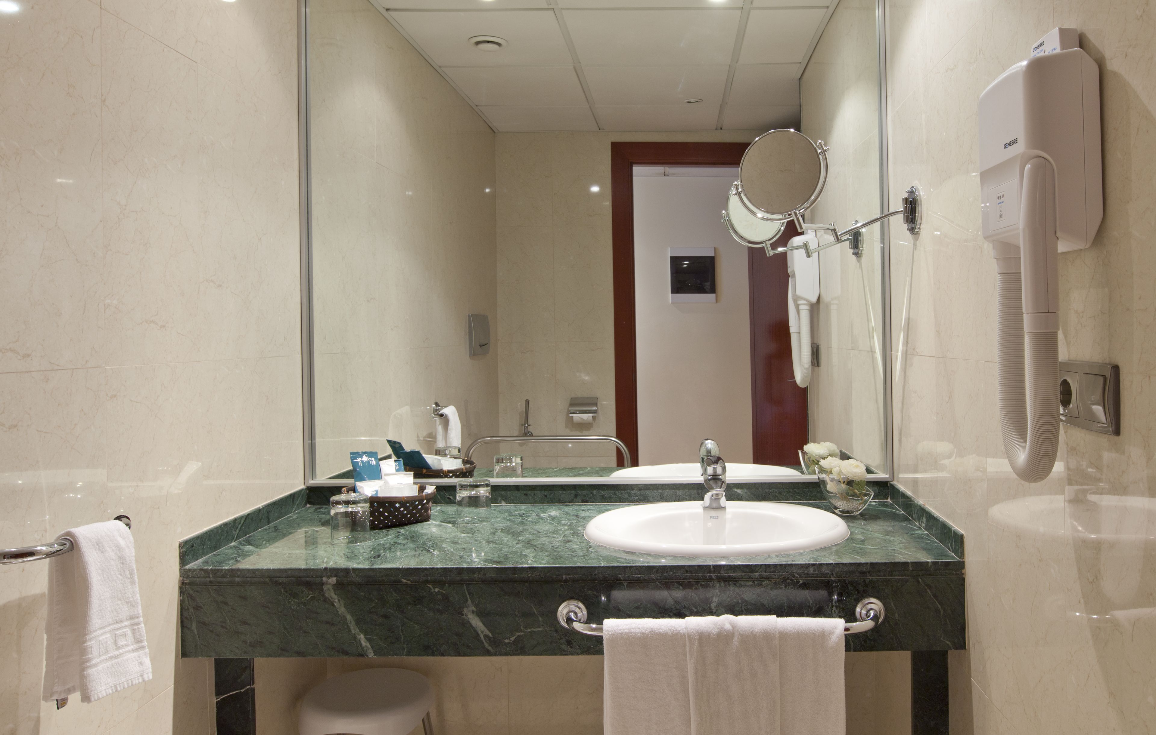 A modern bathroom with a marble countertop, dual sinks, a large mirror, and a handheld showerhead.