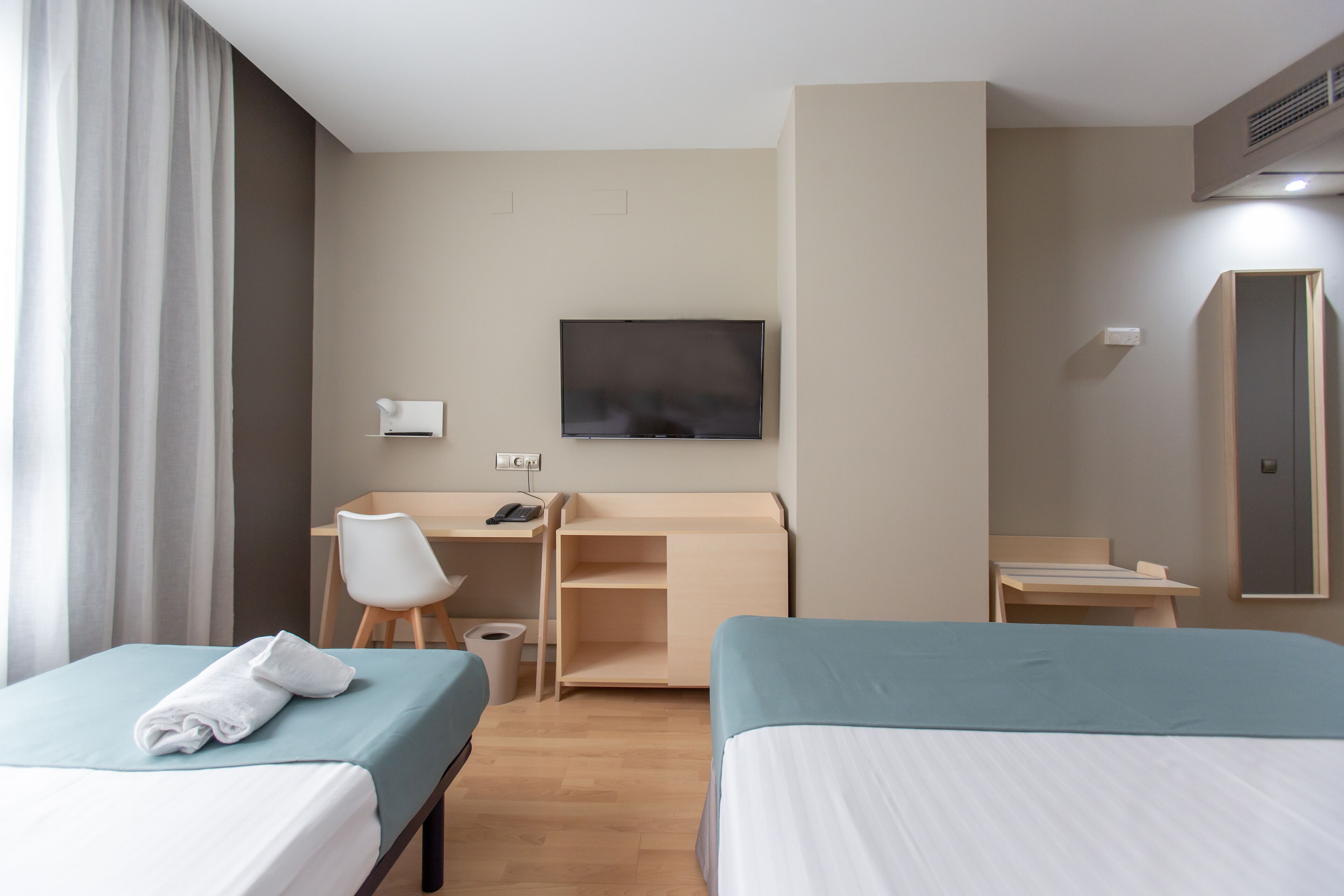 A hotel room with two beds, a desk, a chair, a TV, and a wardrobe.