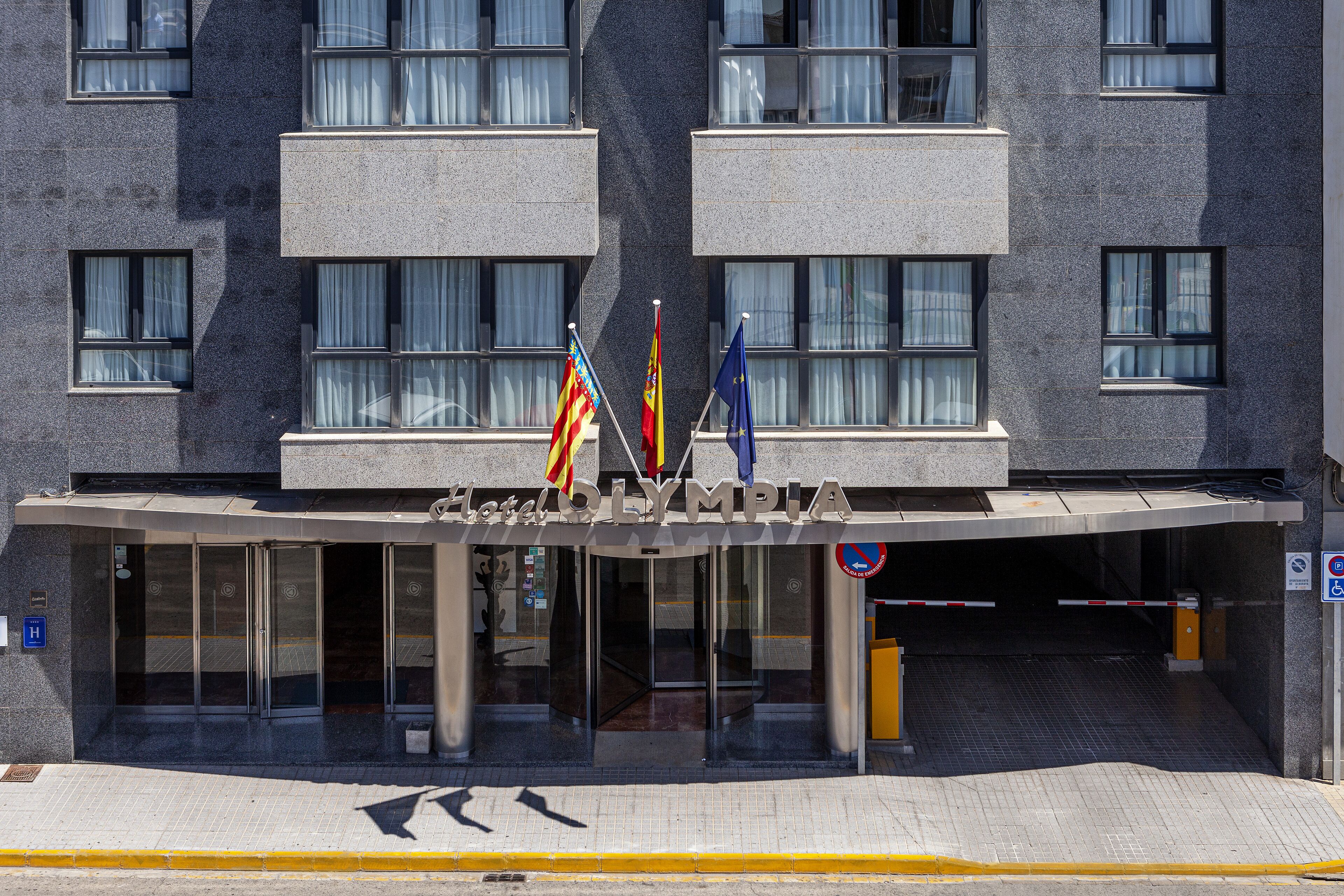 Fachada de hotel de diseño moderno, con cristal, un par de puertas dobles y tres banderas.