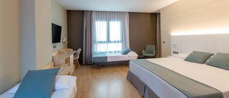 A hotel room with two single beds, a desk with a chair, a television, and a window with curtains.