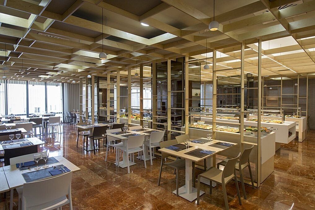 A modern restaurant with a geometric ceiling design, marble flooring, and a variety of seating arrangements.