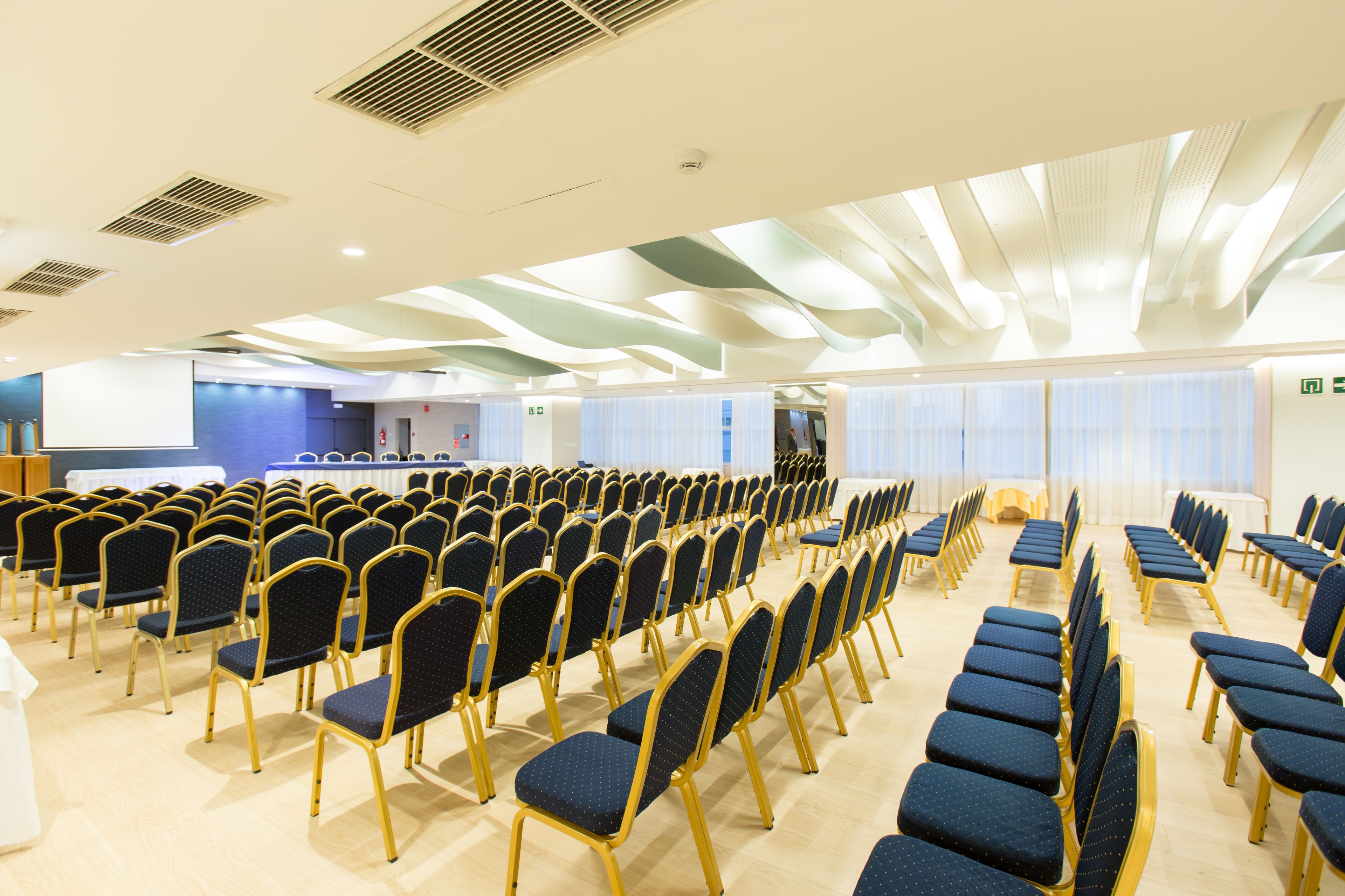 Un salón de conferencias con filas de sillas, un atril y una pared azul con una mesa blanca.