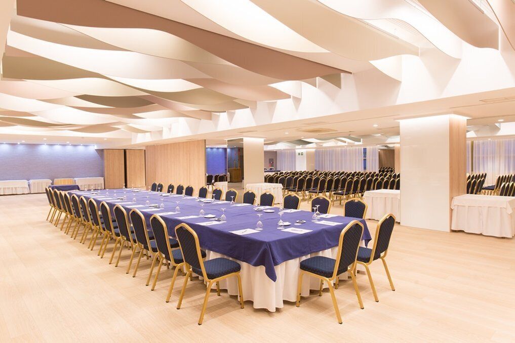 A conference room with long tables and chairs, a modern ceiling design, and a neutral color scheme.