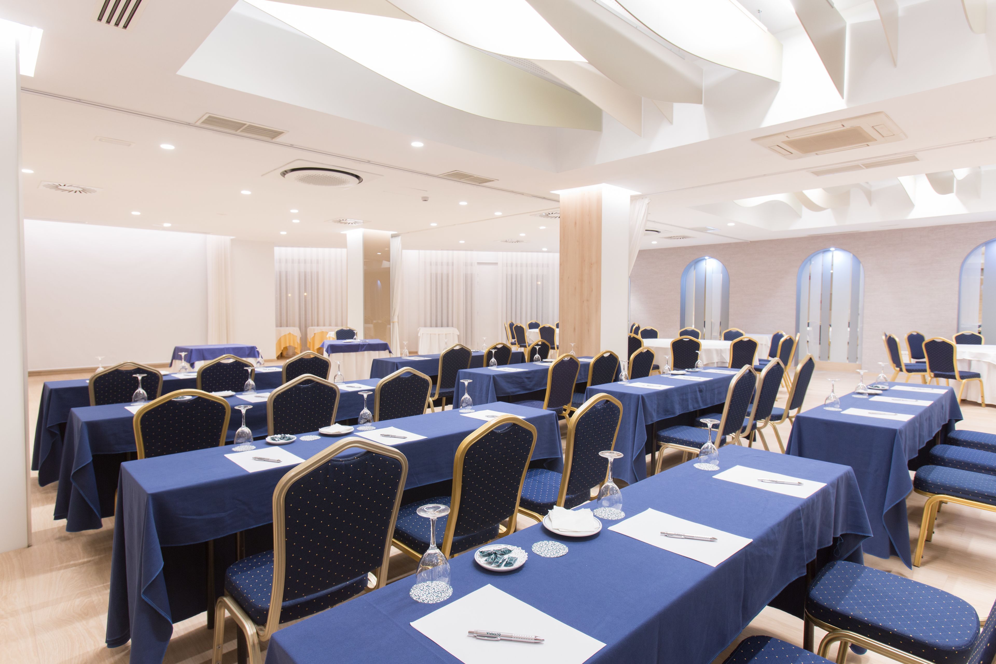 A conference room with multiple tables and chairs, arranged in rows.