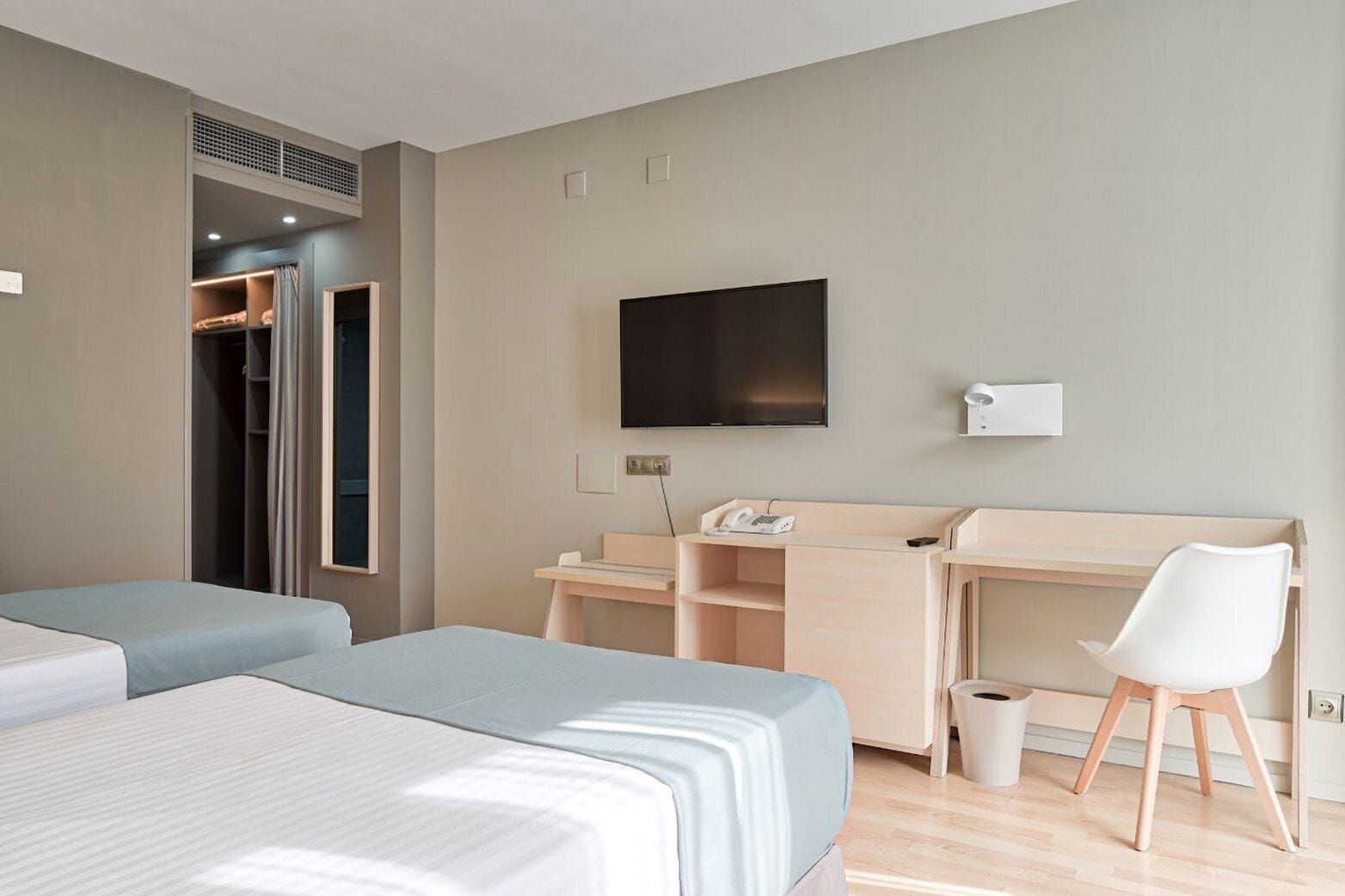 A hotel room with two beds, a desk, a chair, a TV, and a phone.