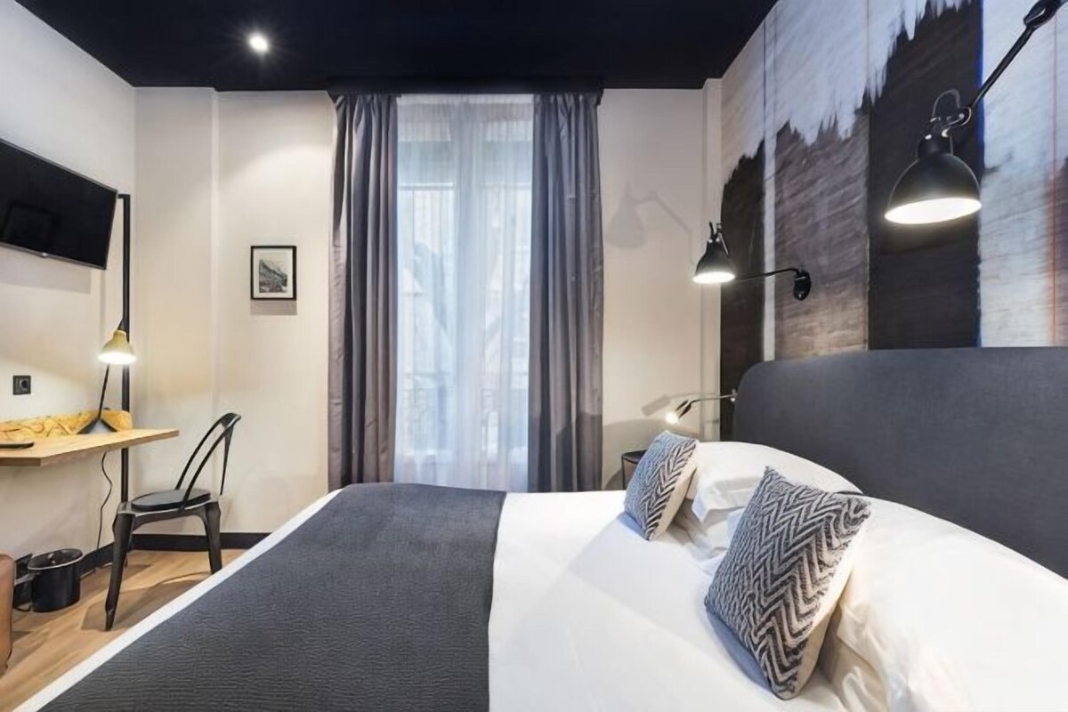 Quarto de hotel moderno com uma cama grande, uma escrivaninha e uma cadeira.