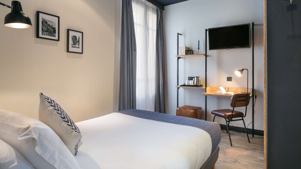 A hotel room with a bed, a desk, a chair, a TV, and a window with curtains. - Hôtel So'Co by HappyCulture (Nice)