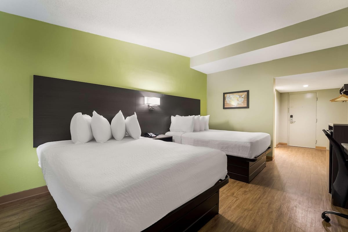 Ein Hotelzimmer mit zwei Betten, einem Schreibtisch, einem Stuhl, einem Kleiderschrank und einer Tür.