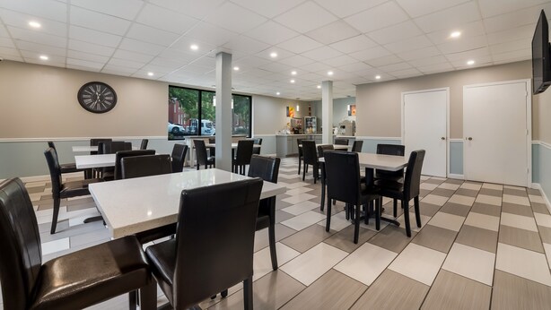 A clean, well-lit indoor space with multiple tables and chairs, a clock on the wall, and a large window providing a view of the outside. - SureStay Hotel by Best Western Columbus Downtown (Columbus)