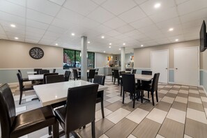 A clean, well-lit indoor space with multiple tables and chairs, a clock on the wall, and a large window providing a view of the outside. - SureStay Hotel by Best Western Columbus Downtown (Columbus)