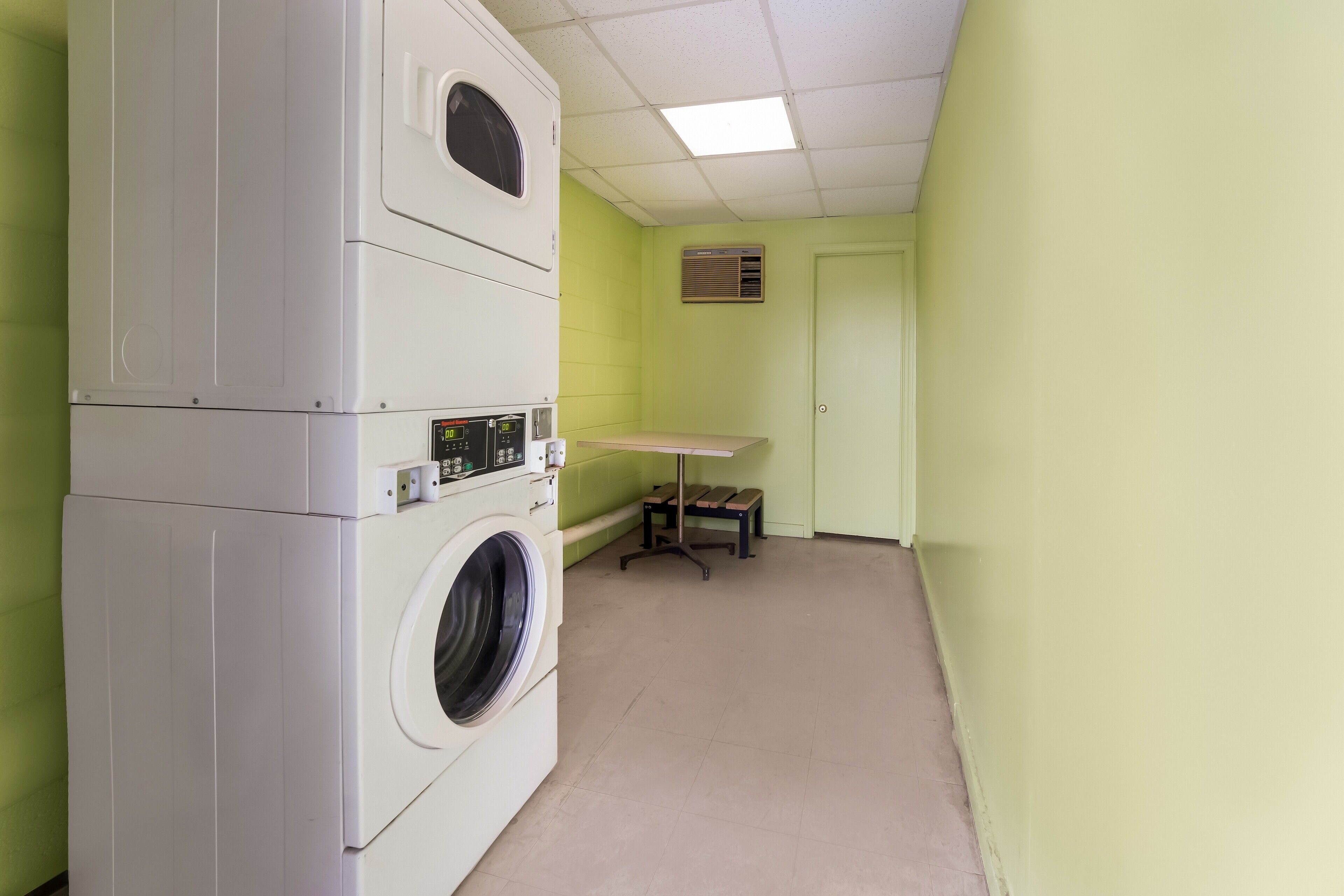 A laundry room with stacked washers and dryers, a table, and a door.