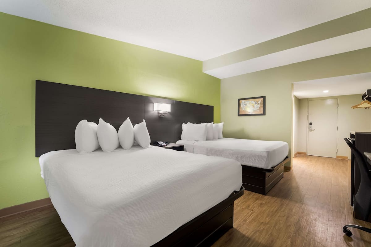 A hotel room with two beds, a desk, a chair, a coat rack, and a door.