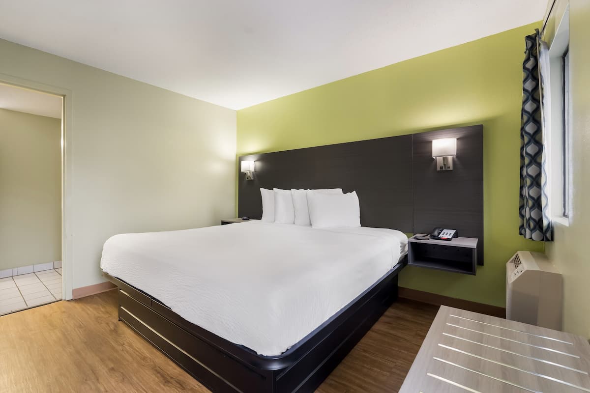 A hotel room with a large bed, a bedside table with a phone, and a wall-mounted light fixture.