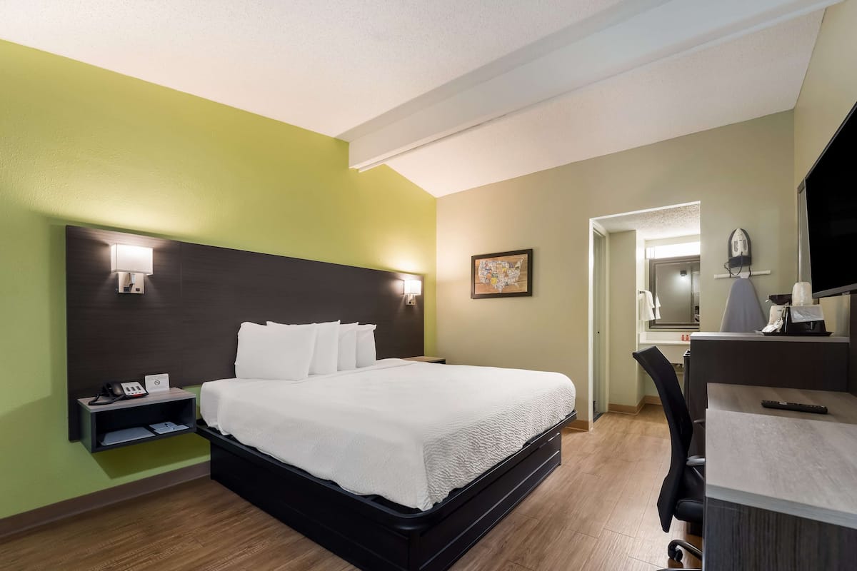 A hotel room with a bed, bedside table, lamp, and a desk with a chair.