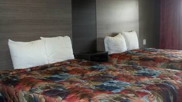 A hotel room with a large bed, two white pillows, a colorful floral bedspread, and a dark headboard.