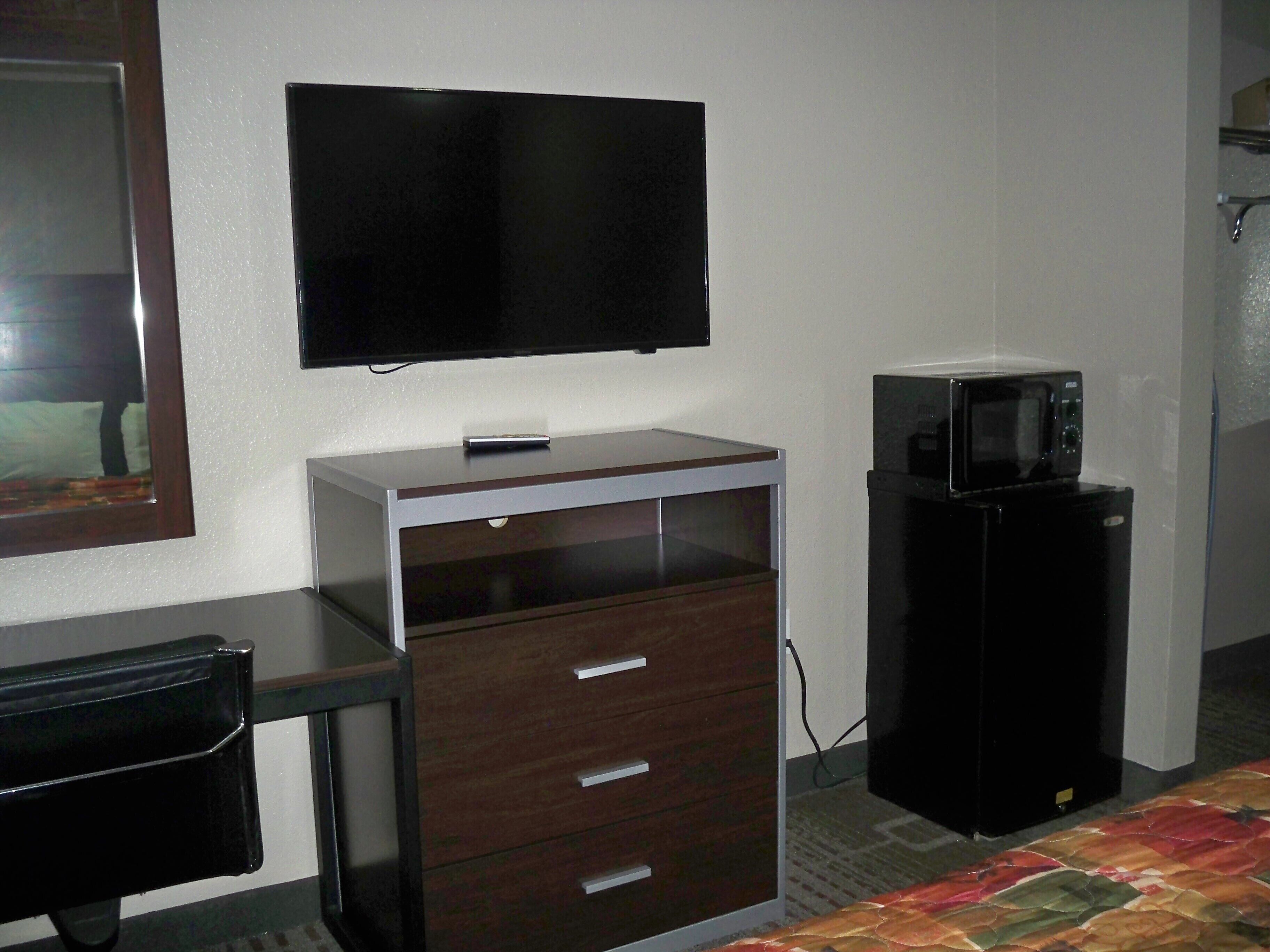 A small room with a bed, a desk, a television, and a microwave.