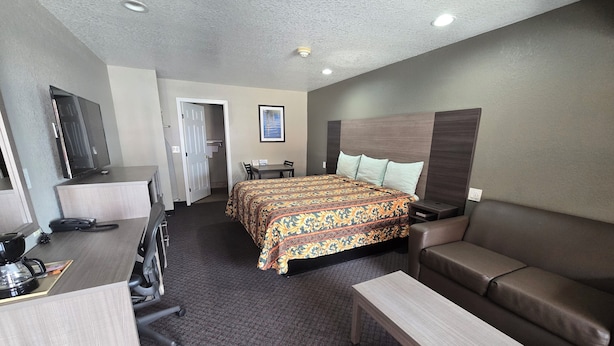 A hotel room with a bed, a sofa, a desk with a chair, a television, and a door. - Scottish Inn & Suites (Beaumont)