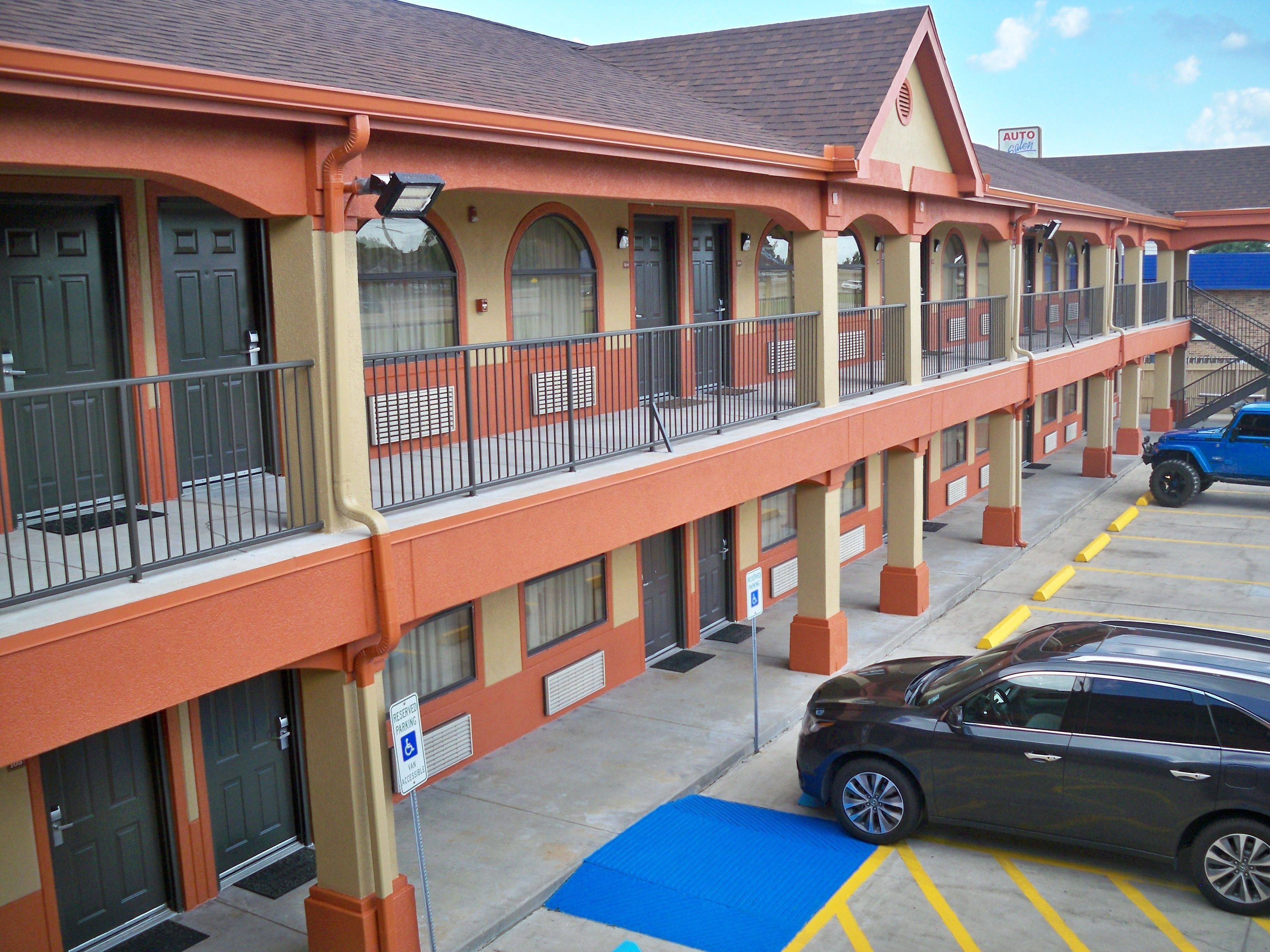 A motel with a two-story structure, featuring balconies, a parking area, and a blue handicapped parking space.