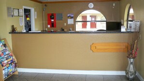 A reception area with a counter, a clock, a fire alarm, and a vase with flowers. - Scottish Inn & Suites (Beaumont)
