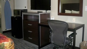 A hotel room with a bed, a desk with a chair, a television, a microwave, and a small refrigerator. - Scottish Inn & Suites (Beaumont)