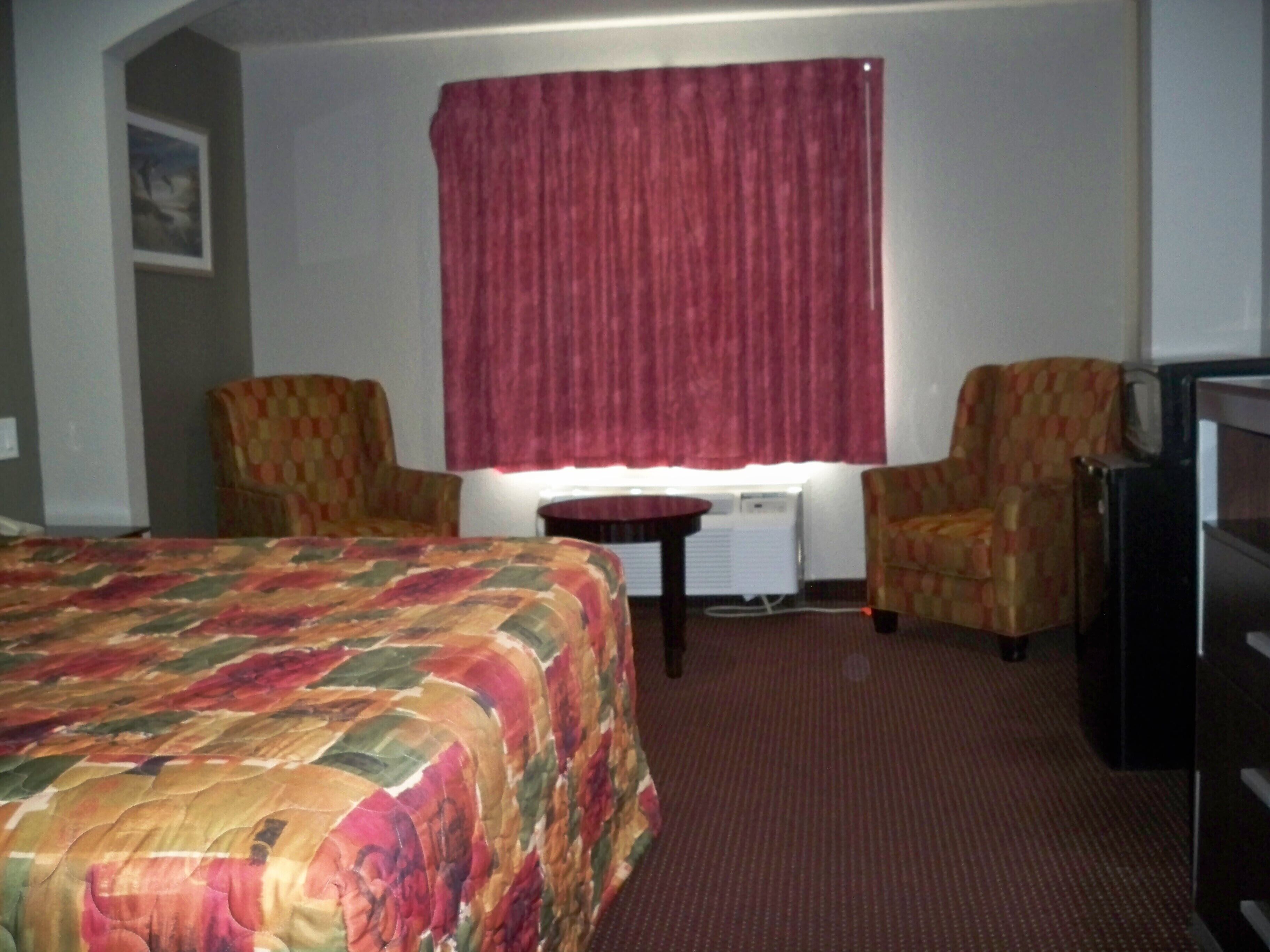 Une chambre d’hôtel avec un grand lit, deux fauteuils, une petite table, un téléviseur et une fenêtre avec un rideau rouge.