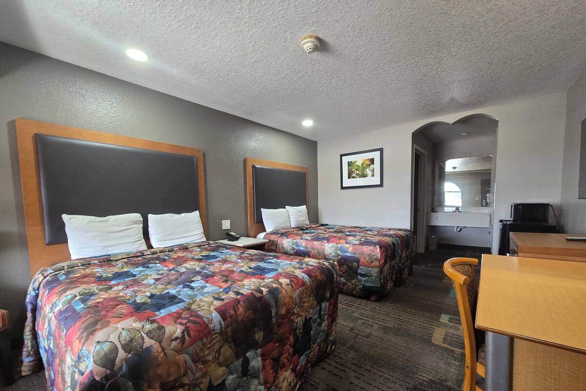 A hotel room with two beds, a desk, a chair, a small table, a picture on the wall, and a ceiling light.