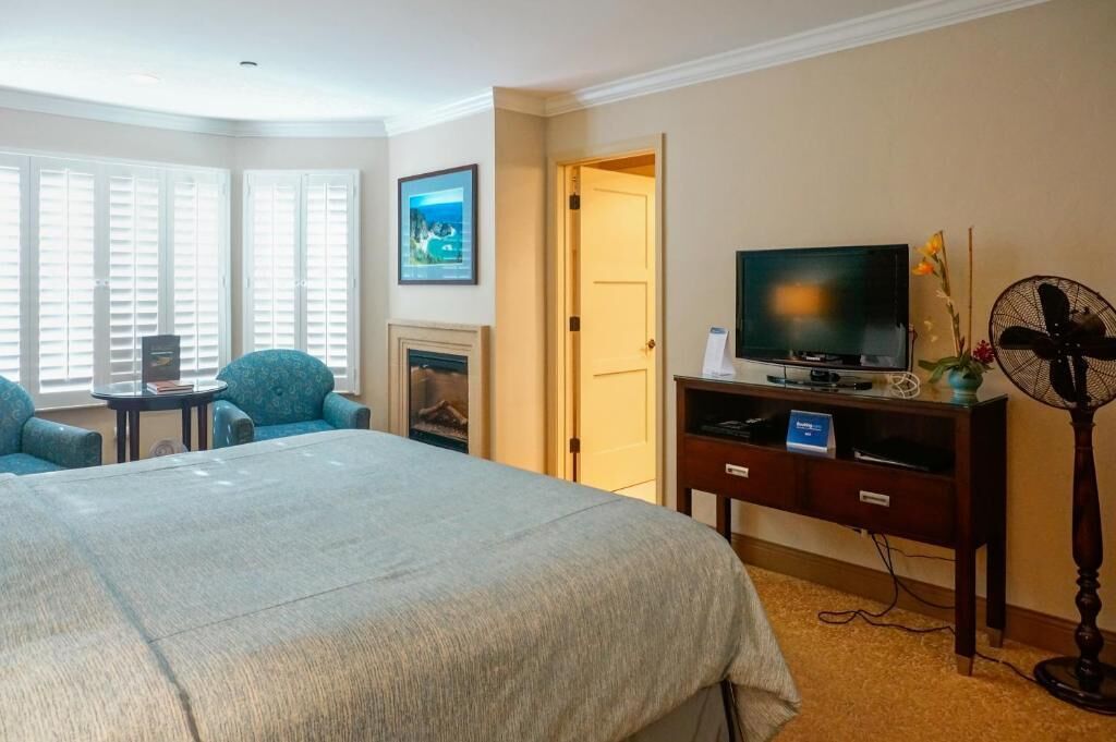 A hotel room with a large bed, a TV, a desk with a chair, a fireplace, and a fan.