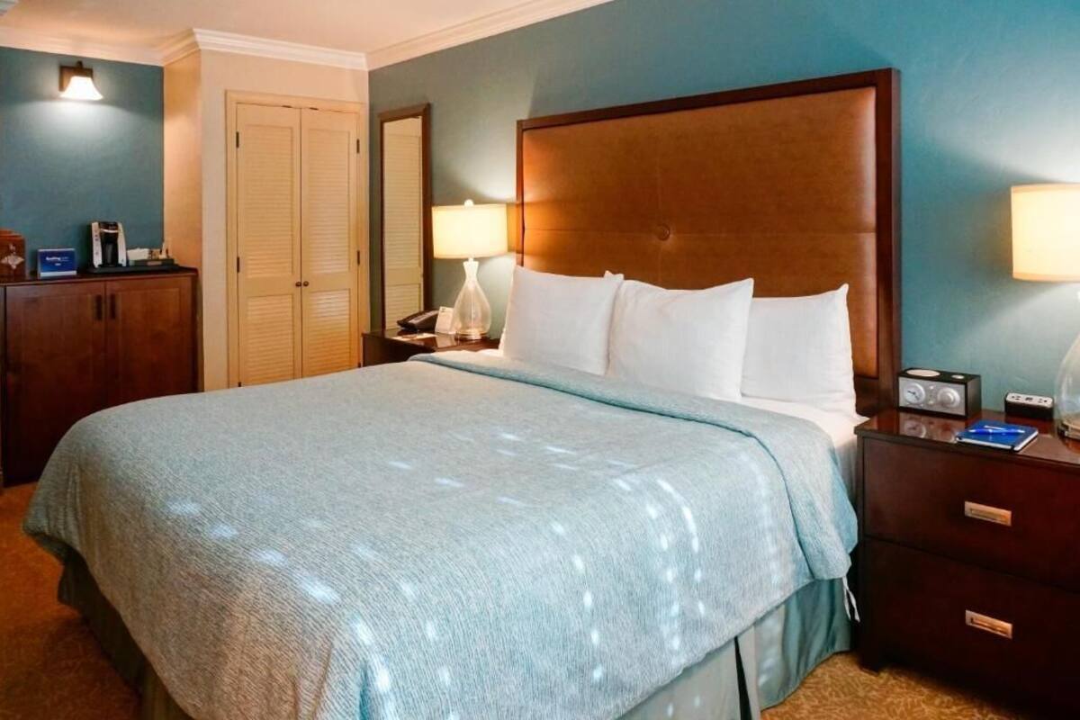 A hotel room with a large bed, a nightstand with a lamp, a dresser, and a closet.