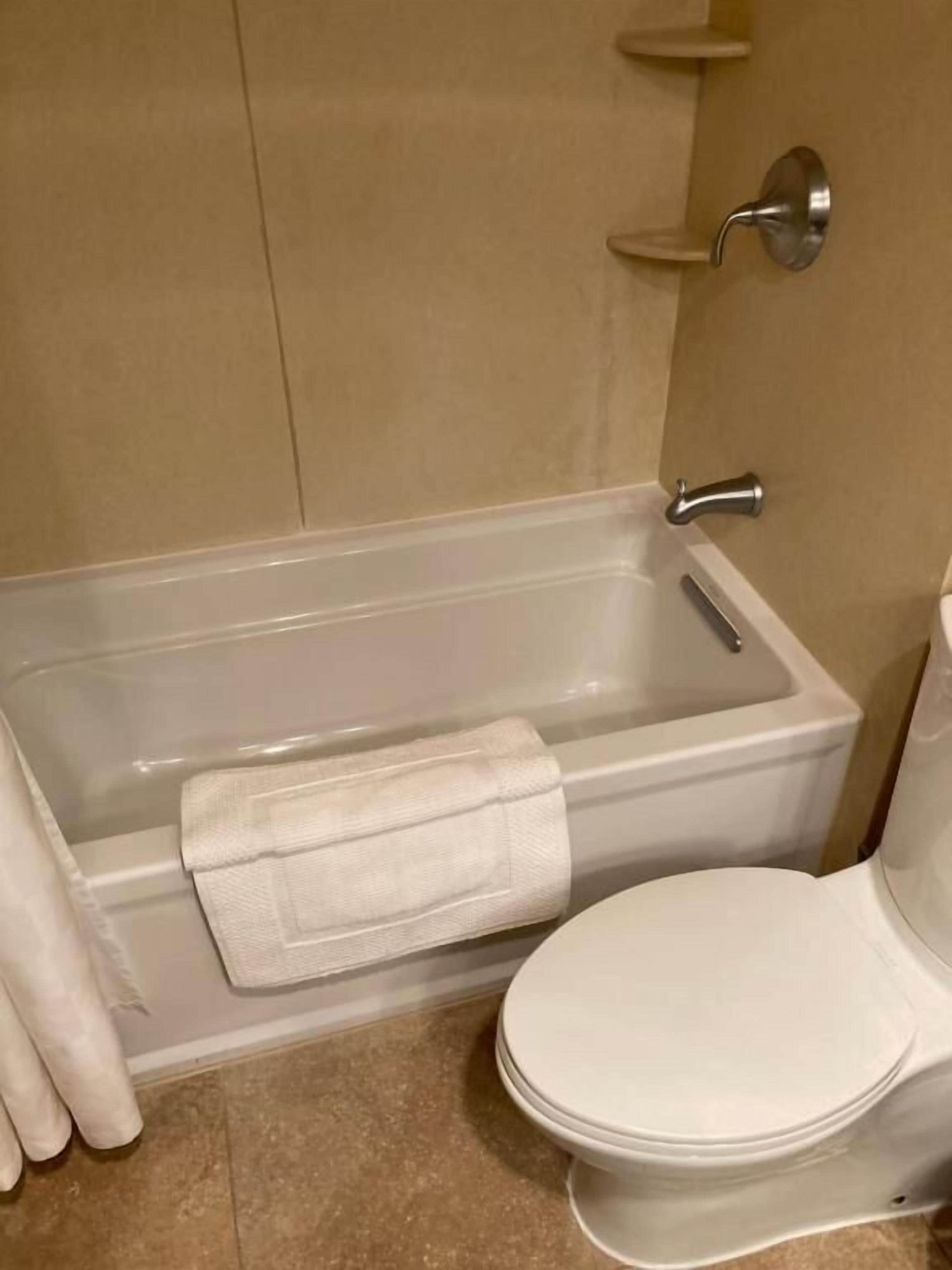 A bathroom with a bathtub, toilet, and a towel placed on the floor.