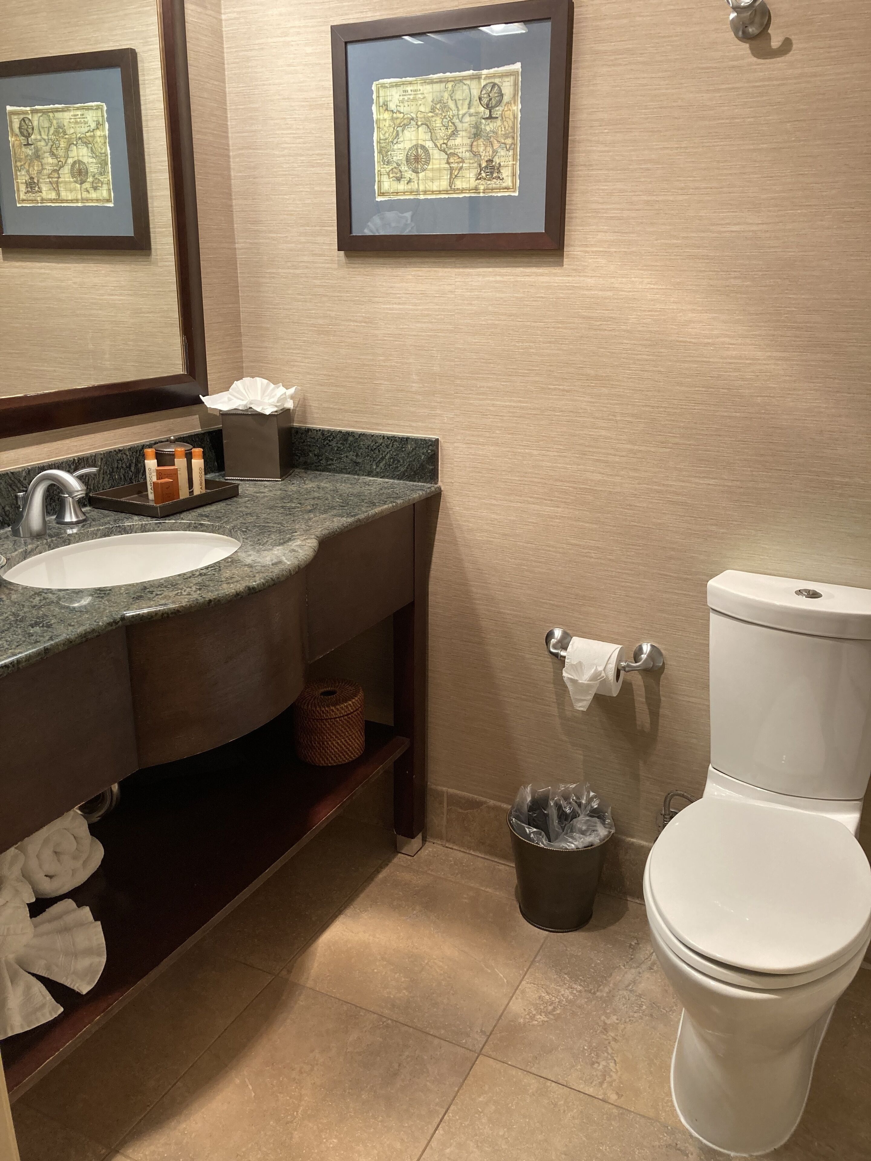 A bathroom with a sink, mirror, toilet, and framed maps on the wall.
