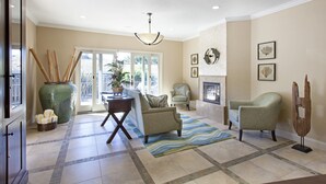 A spacious living room with a large window, a fireplace, and a variety of seating options. - Blue Dolphin Inn (Cambria)