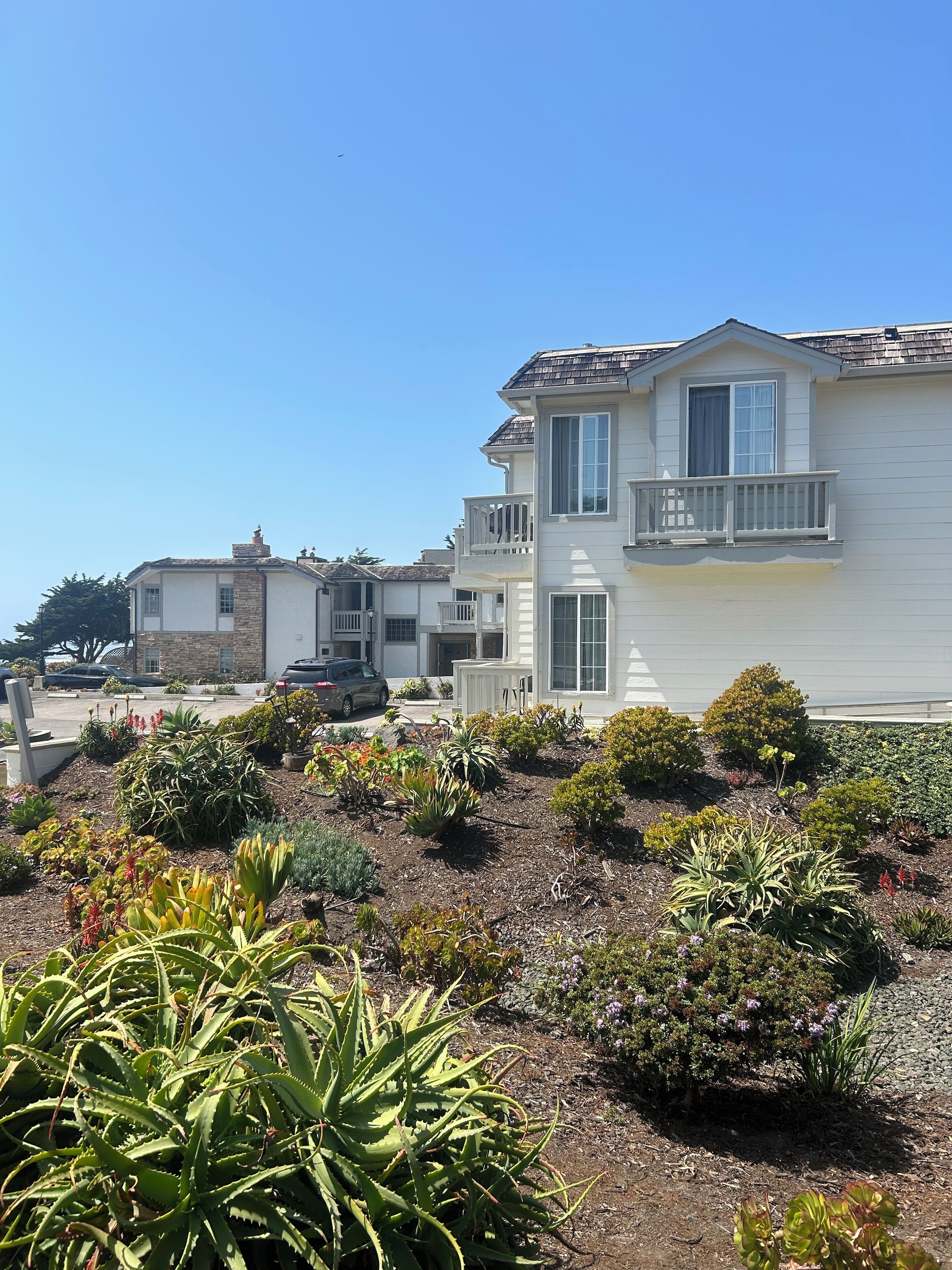 A two-story house with a balcony, surrounded by a landscaped garden with various plants.