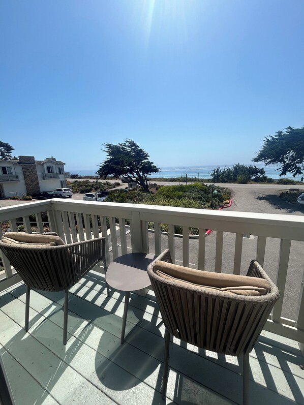A balcony with two wicker chairs and a small table, overlooking a beach and ocean.