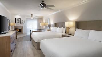 Habitación de hotel con dos camas, una chimenea, un ventilador de techo y un televisor sobre un aparador de madera.