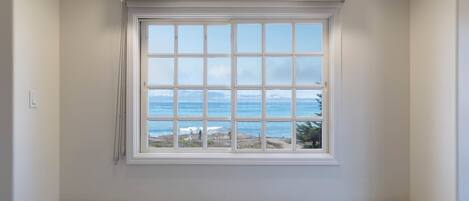 A room with a large window overlooking the ocean, a built-in bench, and recessed ceiling lighting.