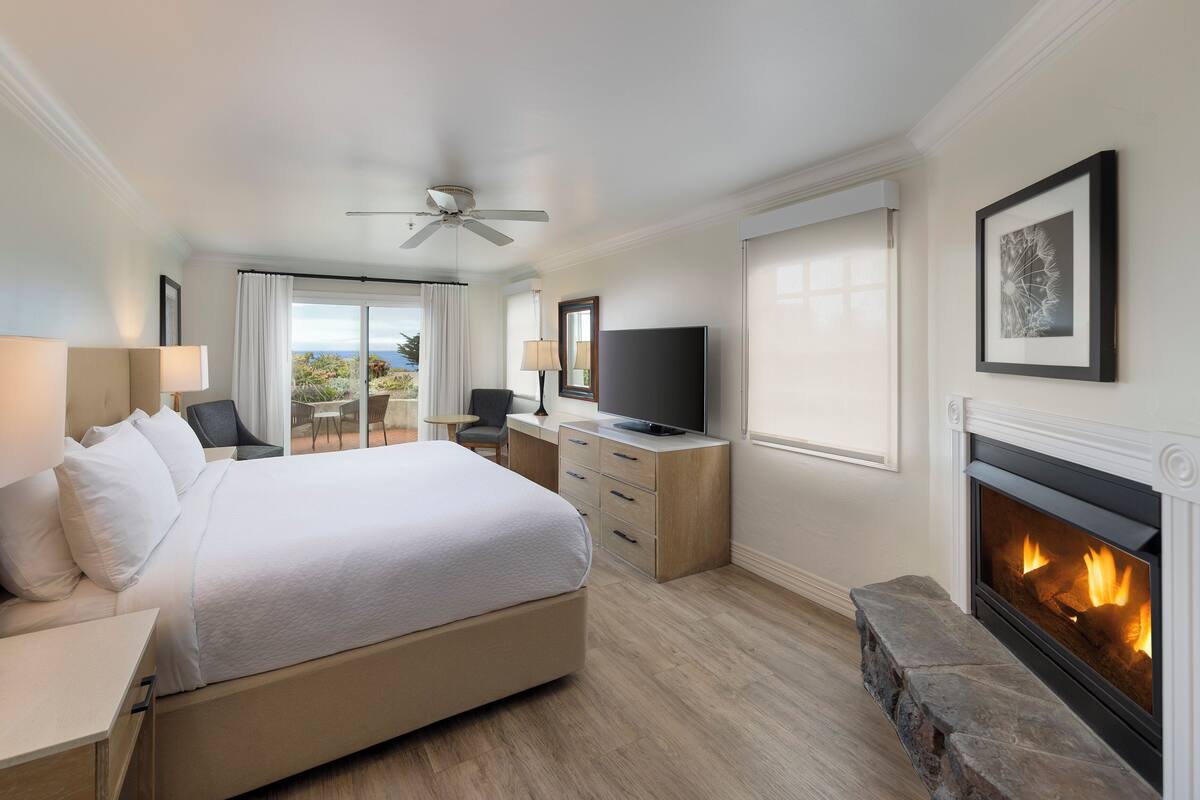 A hotel room with a large bed, a television, a fireplace, and a balcony with curtains.