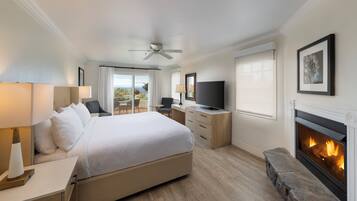 A hotel room with a large bed, a television, a fireplace, and a balcony with curtains.