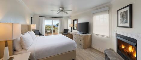 A hotel room with a large bed, a television, a fireplace, and a balcony with curtains.