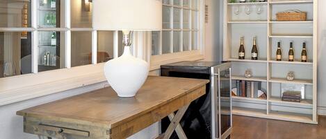 Ein Zimmer mit Holztisch, Lampe und Weinkühler mit Flaschen und Gläsern.