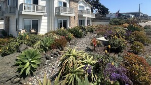 Une maison à deux étages dotée d’un balcon, entourée d’un jardin aménagé avec différentes espèces de plantes et offrant une vue sur l’océan.