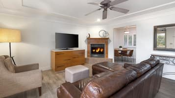A living room with a leather sofa, a television, a fireplace, and a dining area with a table and chairs.