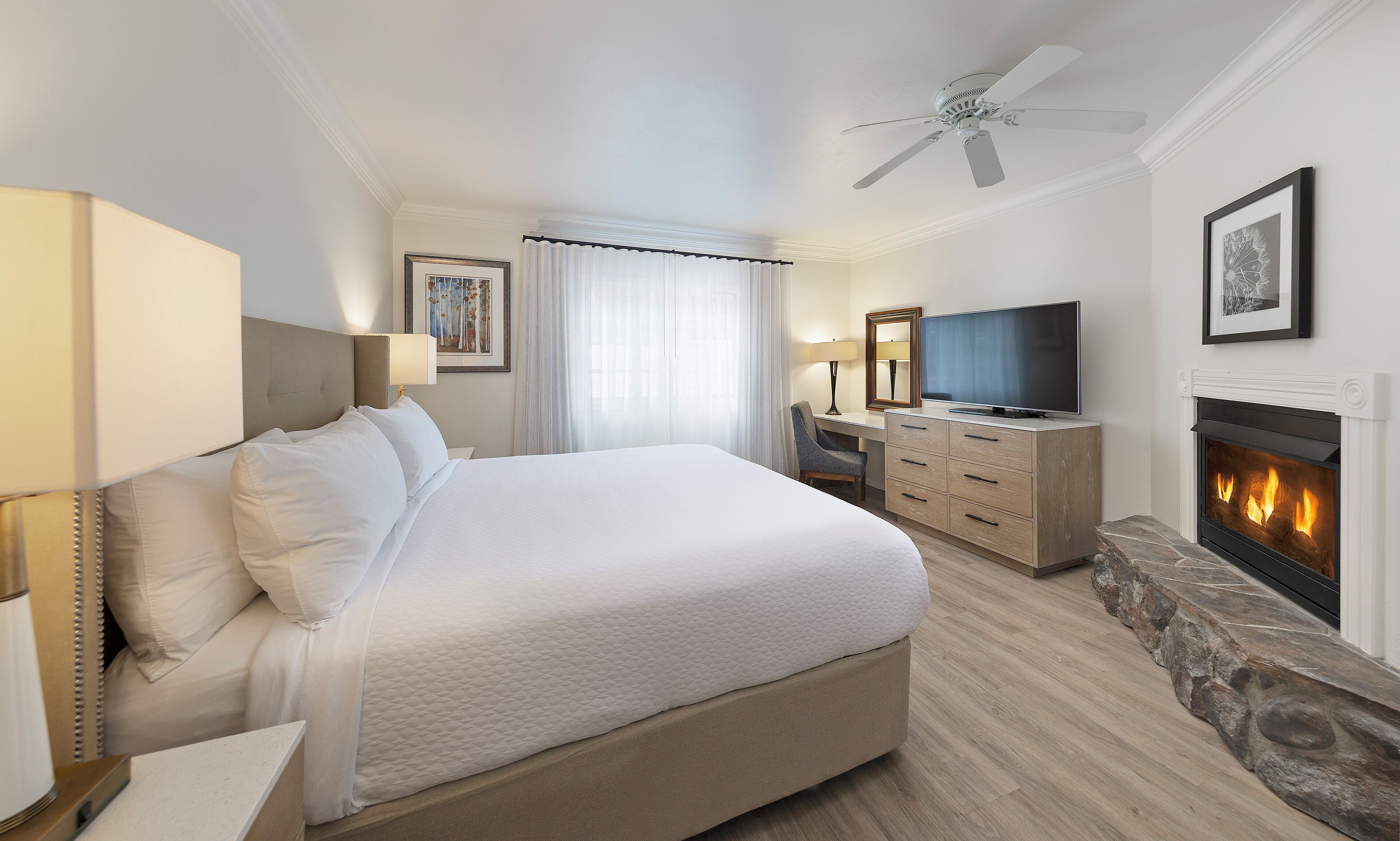 A hotel room with a large bed, a desk, a television, and a fireplace.