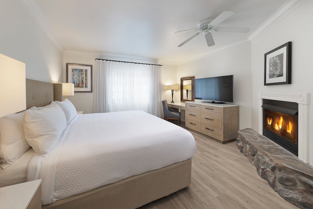 A hotel room with a large bed, a desk, a television, and a fireplace.