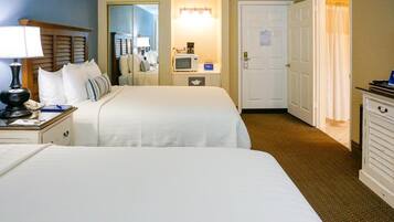 A hotel room with two beds, a bedside table with a lamp, a microwave, and a small desk with a computer.