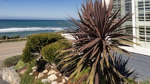A house with a view of the ocean, a garden with rocks and plants, and a clear blue sky.