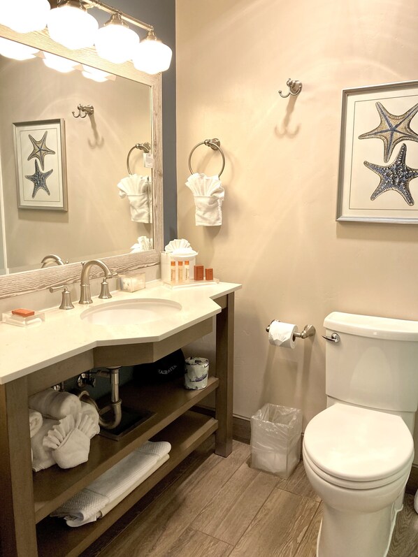 A bathroom with a sink, mirror, towel rack, toilet, and a framed starfish artwork on the wall.