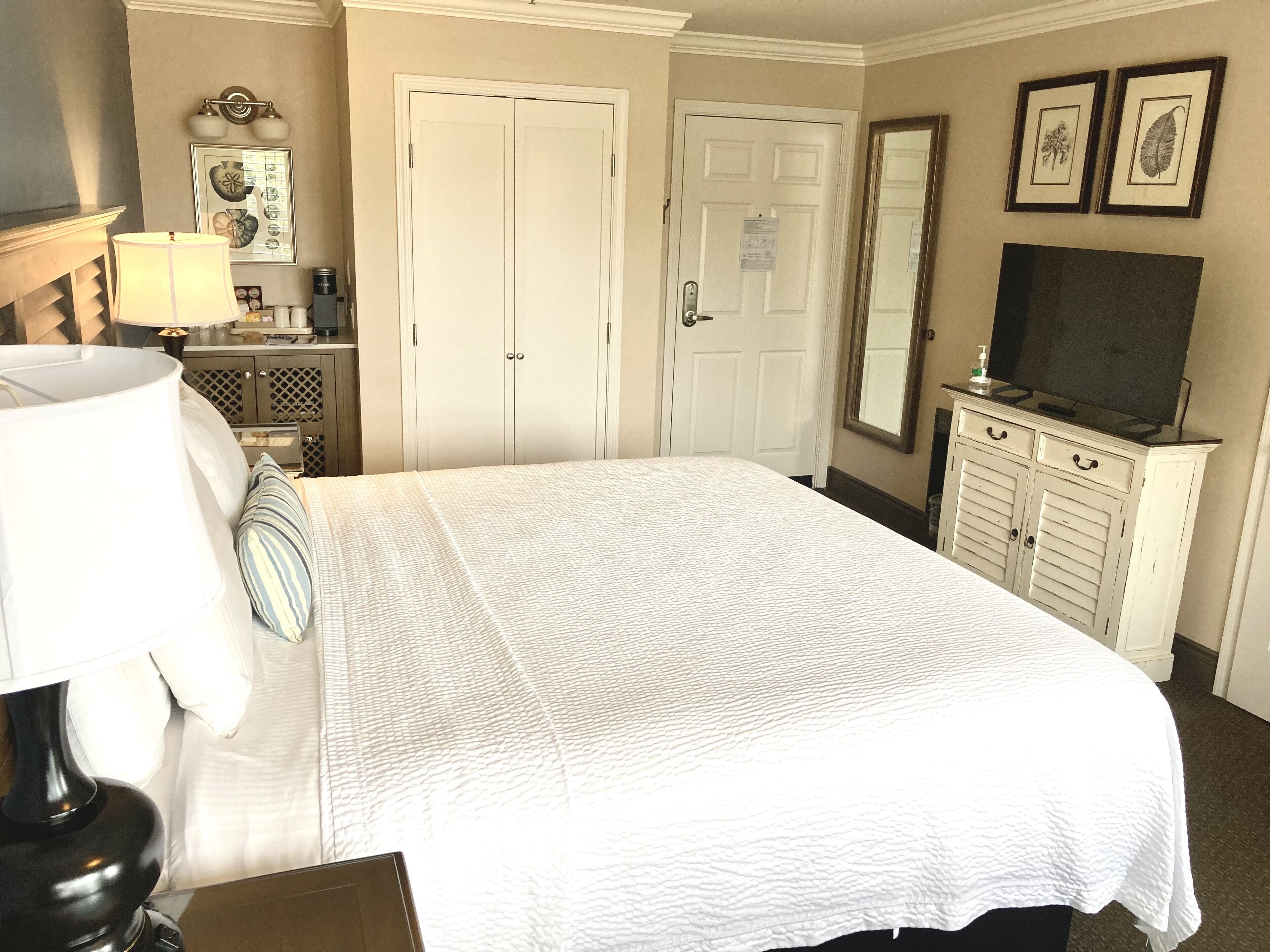 A neatly arranged hotel room with a large bed, a television, a dresser, and a mirror.