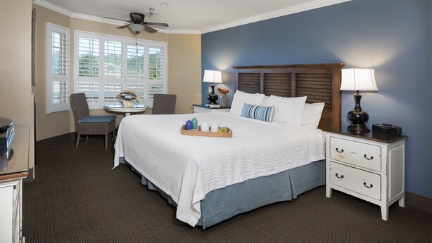 A hotel room with a large bed, a desk, and a chair. There are two nightstands with lamps and a ceiling fan.